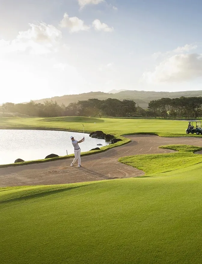 A golfer playing out of a bunker beside a lake on the golf course